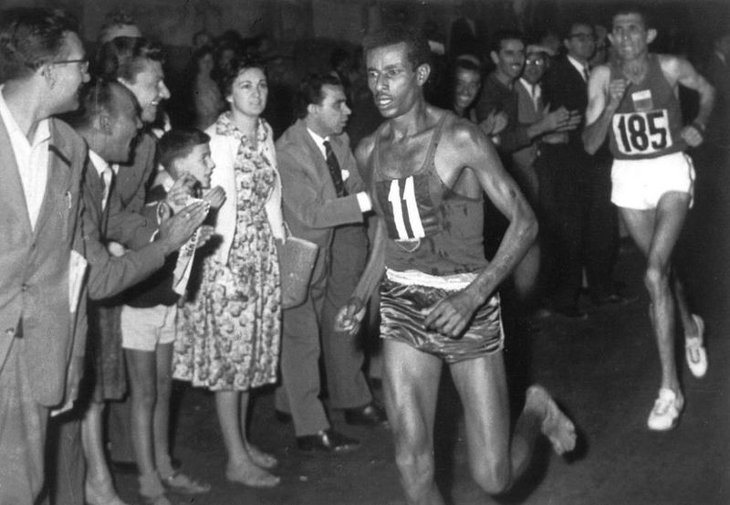 Abebe Bikila running barefoot to Olympic marathon victory, legendary endurance athlete in historic race.