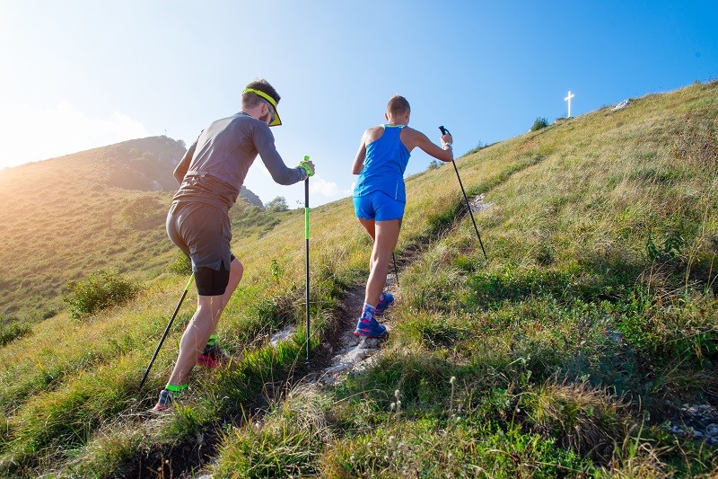 Trail runner choosing lightweight running poles for steep climbs and ultramarathon performance on rocky trail.